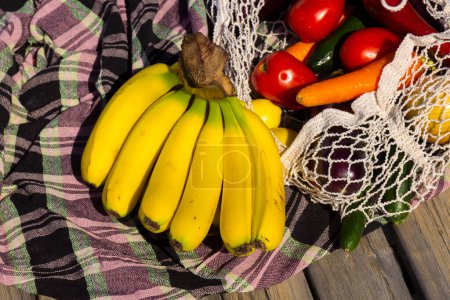 Variedad de frutas y verduras orgánicas frescas en avoska en el mantel en el día soleado. Plátano, zanahoria, tomate en bolsa de hilo. Concepto de alimentación saludable. Enfoque selectivo. Fondo borroso.