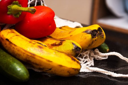 Primer plano de frutas y verduras orgánicas frescas en avoska en la mesa de la cocina. Plátano, pepino y pimienta en una bolsa de hilo. Enfoque selectivo. Fondo borroso.
