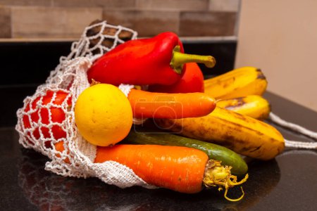 Variedad de frutas y verduras orgánicas frescas en avoska en la mesa de la cocina. Plátano, limón, zanahoria, pepino y pimienta en una bolsa de hilo. De cerca. Enfoque selectivo. Fondo borroso.
