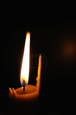 Photo for One waxy candle burns in the dark casting a red glow. Concept photo for mournful occasion - Royalty Free Image