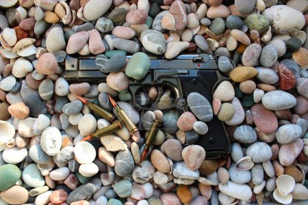 Photo for Pistol Gun Sprinkled With Smooth Stones And Scattered Bullets Top View - Royalty Free Image
