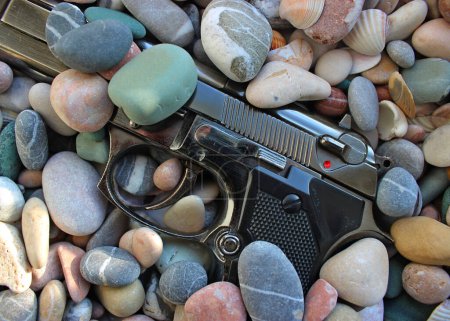 Photo for Discarded Automatic Pistol Half Buried Gun Round In Round Sea Stones - Royalty Free Image