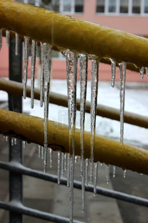 Transparent icicles on the painted railing of a house in the city 