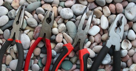 Photo for Top parts of variety types of pliers lined up in size comparison on a round smooth rocks concept photo for background or wallpapers - Royalty Free Image
