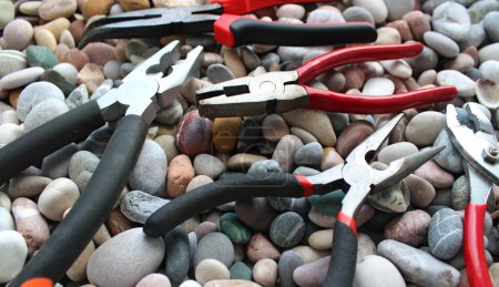 Téléchargez les photos : Différents types de pinces avec poignées caoutchoutées disposées sur une vue d'angle des pierres de mer - en image libre de droit