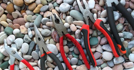 Photo for Stock Photo Of Slip Joint Pliers, Groove Pliers, Needle Nose Pliers And Linesman Pliers In Size Order On A Pebble Stones - Royalty Free Image