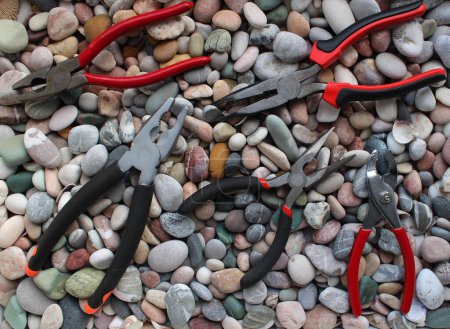Photo for Kit Of Variety Pliers With Opened Jaws Laid Out On A Colorful Pebbles Stock Photo For Backgrounds Or Wallpaper - Royalty Free Image