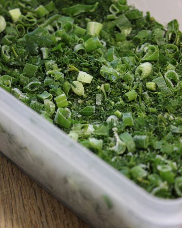 Photo for Home Cooking Ideas. Plastic Box With Finely Chopped Unfrozen Parsley, Dill And Onions Prepared To Cooking - Royalty Free Image