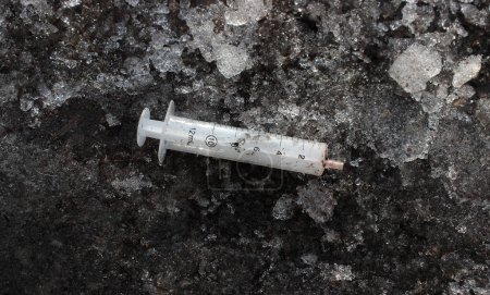 Téléchargez les photos : Danger d'infection seringue en plastique est piétiné dans le sol gelé avec des éclats de glace - en image libre de droit