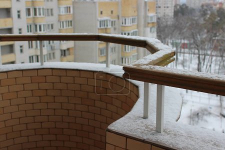 Invierno en la ciudad foto de stock. Nieve ligera en la barandilla del balcón abierto de un edificio residencial de gran altura