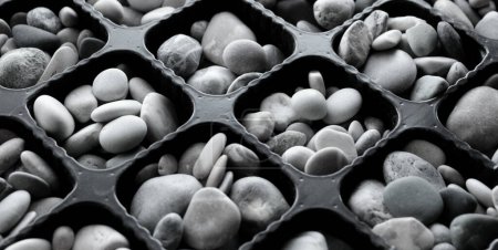 Symmetrische Trennwände mit gleichen Zellen gefüllt mit glatten Ziersteinen Schwarz und Weiß Archivfoto  
