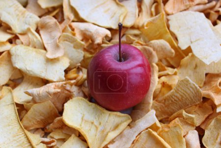 Téléchargez les photos : Photo de stock d'une pomme fraîche allongée sur des chips de pommes de friteuse à air pour illustrer des bonbons de pommes faits maison - en image libre de droit
