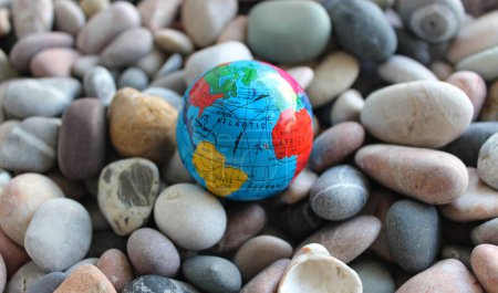 Miniaturglobus auf einem Meeresstein mit konventionell gezeichneten Kontinenten, Ozeanen und Handelswegen darauf