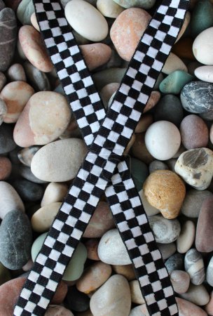 Gekreuztes schwarz-weißes kariertes Band auf glatten Steinen. Konzeptfoto zur Illustration Wettbewerb Zielflagge  