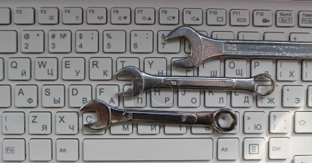 Engineering And Computer Hardware Concept. Three shiny mechanical wrenches laid out in order on computer keyboard top view