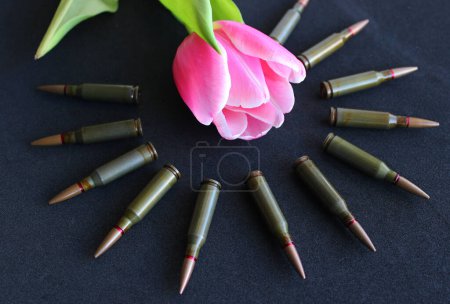 Konzeptfoto zum Thema Trauer und Ehrung der Kriegsopfer. Tulpe und Kugeln drumherum auf schwarzem Hintergrund