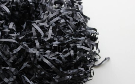 Ein Bündel aus schwarzem, geschreddertem Papier auf sauberer weißer Oberfläche. Textur von Papierspänen Detailliertes Archivfoto