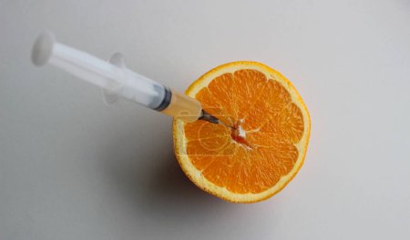 Foto de Contenido de vitaminas en las frutas. La mitad de una naranja madura cortada con una aguja de jeringa clavada en la pulpa jugosa de la fruta - Imagen libre de derechos