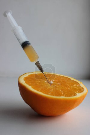 Eine Spritze mit frischem Saft aus einer reifen, halbierten Orange. Vertikales Archivfoto zur Illustration der Lebensmittelanalyse