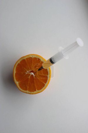 Eine Spritze, die zur Hälfte mit Orangensaft gefüllt ist, wird in eine saftige, halbierte Orange eingeführt. Obsttest und gentechnikfreies Konzept 