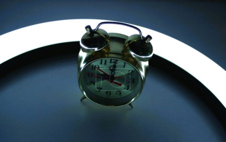Horloge classique en cuivre avec cloches sur une table de nuit avec lampe à anneau LED dans l'obscurité 