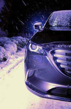 Winterliche Autosicherheit und Straßenverhältnisse Archivbild. Schnee auf Außenspiegeln und Windschutzscheibe eines Autos bei nächtlichem Schneefall
