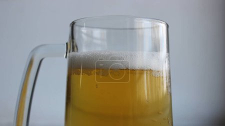 Top part of glass with handle filled of craft brown ale covered with foam closeup view