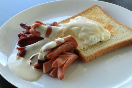 Breakfast plate with sausages under white sauce and poached egg on toasted bread. Classic buffet meal stock photo