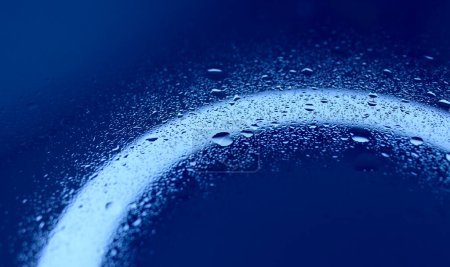 Textur von Spritzwasser auf beleuchteter blauer Glasoberfläche 