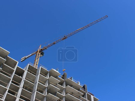 Téléchargez les photos : Cordes d'acier suspendues au bras d'une énorme grue à tour sur le cadre de bâtiment en béton sur le chantier de construction - en image libre de droit