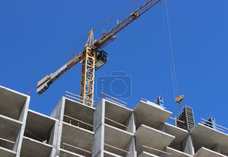 Téléchargez les photos : Une partie de la grue jaune de construction de haute altitude se lève au-dessus des dalles de plancher de béton d'un bâtiment à plusieurs étages au processus de construction - en image libre de droit