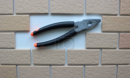Closed Pliers In Clean Compartment Inside Tiles Brickwork Top View. Stock Photo For DIY Works Illustration