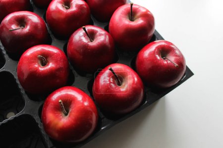 Téléchargez les photos : Fruits rouges parfaits de pomme dans des endroits séparés de la boîte en plastique noire - en image libre de droit