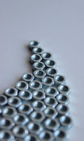 Identical thread nuts are laid out on a white table in the shape of an irregular triangle. Vertical Stock Photo For Fixing Hardware Illustration 
