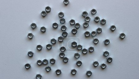 Small steel nuts of the same size are scattered on the scratched surface of a white workbench