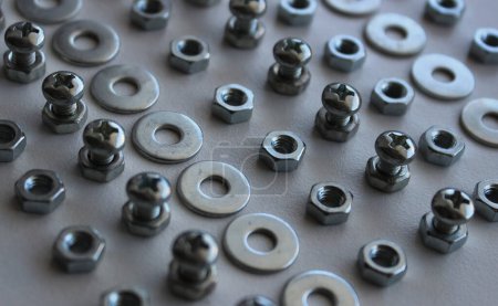 Shiny iron washers, spacers, nuts and bolts arranged in lines on the white plastic sheet. Stock Photo For Fastener Hardware Backgrounds