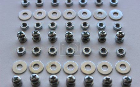Perfectly even rows of steel shiny nuts, bolts and washers on a white surface
