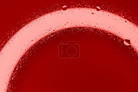 Rote Flüssigkeitstropfen spritzten mit rotem Licht von unten auf eine saubere Oberfläche. Illustratives Archivbild des Kreislaufsystems