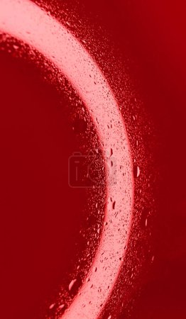 Tropfen auf nasser transparenter Oberfläche mit intensiver roter Hintergrundbeleuchtung. Metaphorisches Archivfoto für den Blutkreislauf