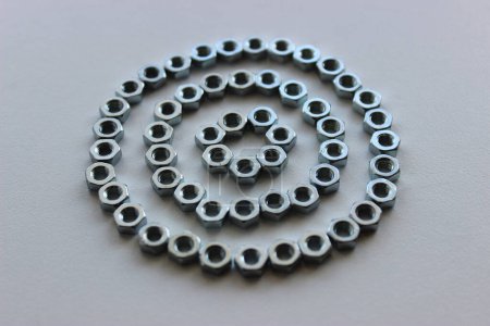 Photo for Three Circles One Inside Another Made With Same Steel Nuts On White Workbench Surface. Hardware Background For Vertical Story - Royalty Free Image