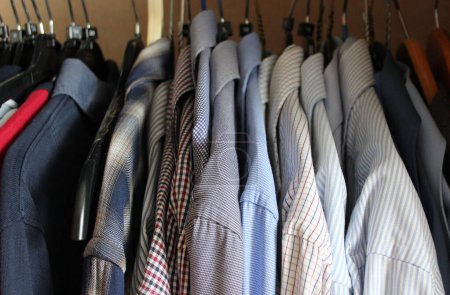 Varias camisas casuales en plástico flocado y perchas de madera en un armario doméstico. Clásico ropa stock foto