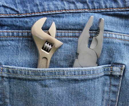 An adjustable spanner and pliers are placed in a jeans pocket. Closeup stock image for home repair theme 