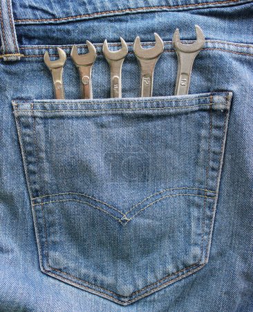 Steel wrenches arranged by size sticking out from the denim pocket. Vertical stock photo for home tools storage theme