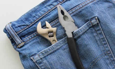 Adjustable wrench and pliers with one untucked handle in a jeans pocket. Detailed stock photo for home tools illustration