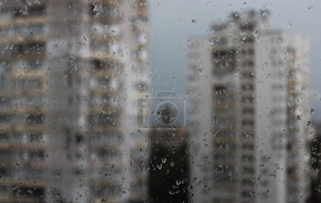 Blick durch nasse Fenster auf verschwommene Mehrfamilienhäuser im Regen