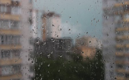 Defokussierte Hochhäuser blicken durch nasses Fensterglas mit Regentropfen