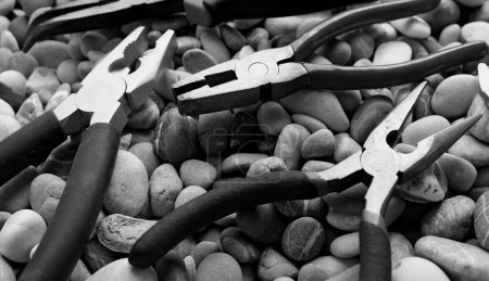 Slip Joint Pliers, Groove Pliers, Needle Nose Pliers And Linesman Pliers Laid Out On Stones Surface Black And White Image
