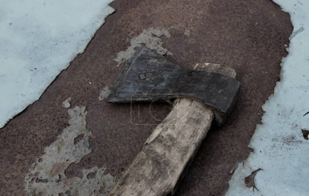 Vintage domestic axe with worn mark on the old wooden handle on rough rusty surface