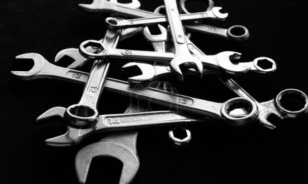 Heap of different size metal wrenches isolated on black sheet angle view closeup photo in black and white style