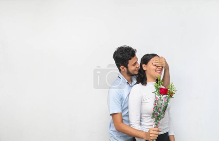 Foto de Joven hombre tapa los ojos de su enamorada para sorprenderla con hermoso ramo de rosas - Imagen libre de derechos